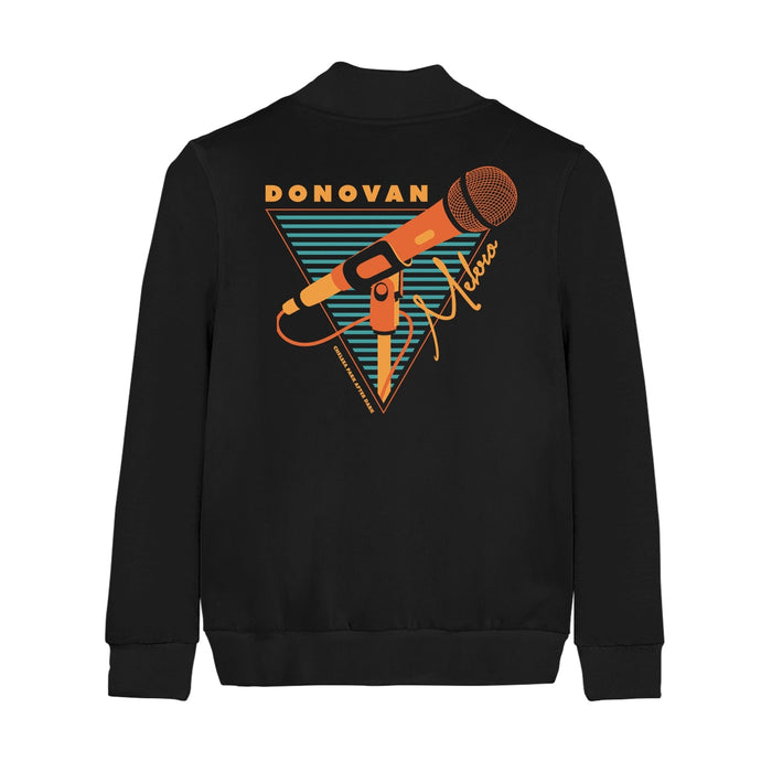 Back of black champion bomber jacket with an orange microphone drawn in the center. Surrounding it is an orange triangle filled with black and teal stripes. On top of the triangle there is orange text that says DONOVAN and on the side there is orange text that says MELERO in cursive.
