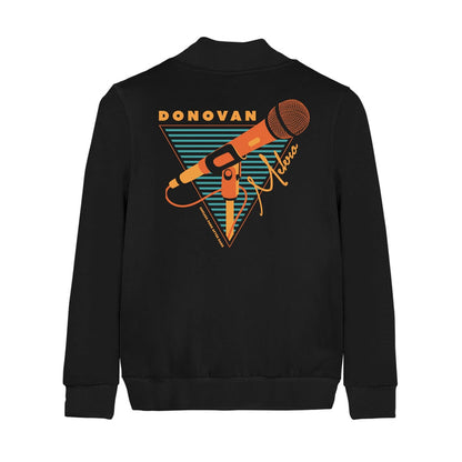 Back of black champion bomber jacket with an orange microphone drawn in the center. Surrounding it is an orange triangle filled with black and teal stripes. On top of the triangle there is orange text that says DONOVAN and on the side there is orange text that says MELERO in cursive.