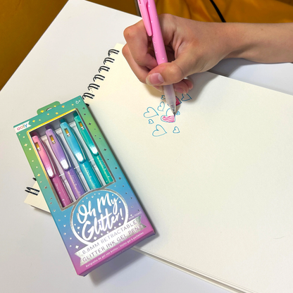 Hand coloring in blue hearts with a pink OOLY Oh My Glitter! Retractable Gel Pen on a sketchpad