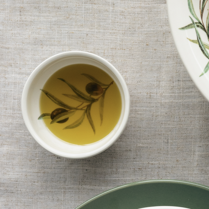 Small ceramic bowl with an olive design filled with olive oil on a linen tablecloth