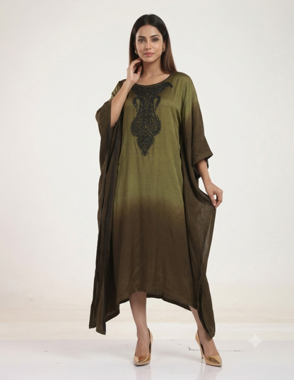 A female model standing against a neutral studio background, wearing an olive-to-brown ombre kaftan dress with intricate black bead embroidery on the neckline, paired with gold heels.