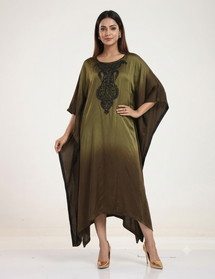 A female model standing against a neutral studio background, wearing an olive-to-brown ombre kaftan dress with intricate black bead embroidery on the neckline, paired with gold heels.