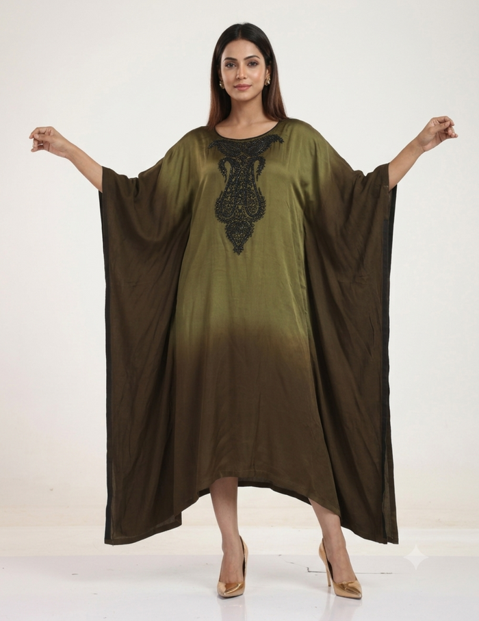 A female model standing against a neutral studio background, wearing an olive-to-brown ombre kaftan dress with intricate black bead embroidery on the neckline, paired with gold heels.