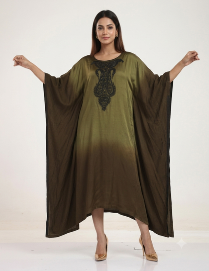 A female model standing against a neutral studio background, wearing an olive-to-brown ombre kaftan dress with intricate black bead embroidery on the neckline, paired with gold heels.