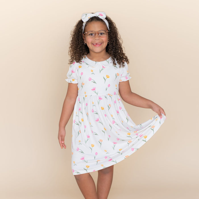 Young girl posing wearing the Peter Pan Collar Dress in Tulip holding the hem of the skirt