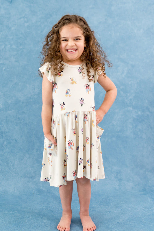 Girl wearing dress with flutter sleeve and pockets in a mickey and friends character pattern with a blue background