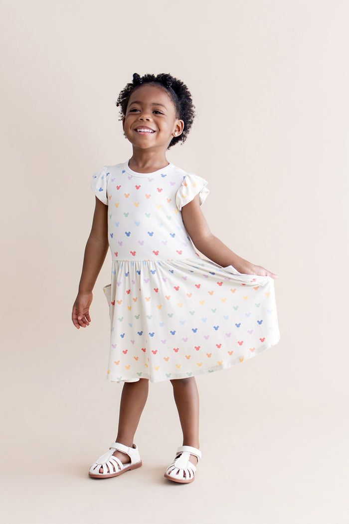 Young girl wearing a cream dress with colorful mickey patterns on a beige background