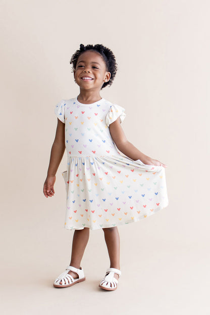 Young girl wearing a cream dress with colorful mickey patterns on a beige background