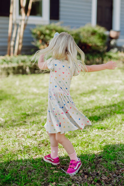Child in a dress with colorful patterns standing on grass in front of a house.