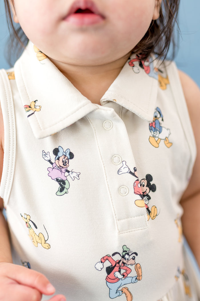 Child wearing a sleeveless dress with cartoon character prints against a blue background