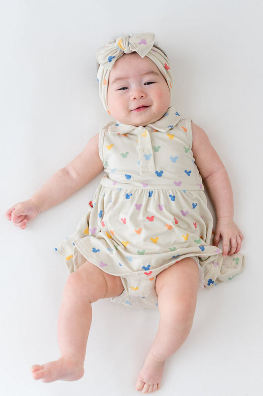 baby in a cream dress with mickey head pattern with a collar and buttons