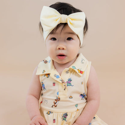 Close up of infant sitting wearing the Polo Bodysuit Dress in Winnie the Pooh Celebration with light yellow bow