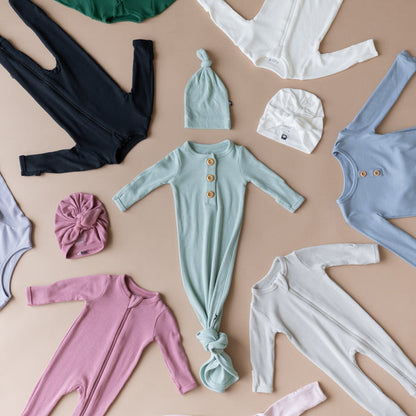 Kyte Baby Ribbed pajamas and headwraps in multiple colors on a light brown surface