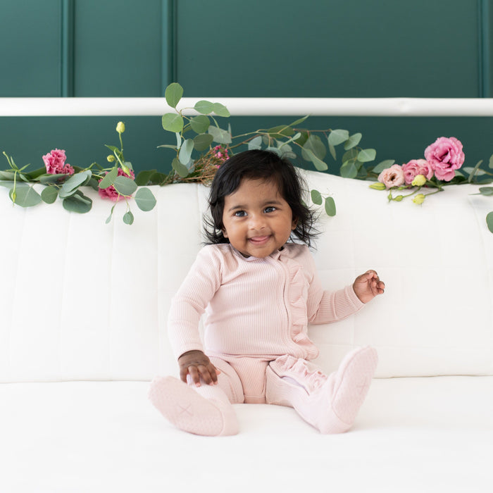 Child wearing Kyte Baby Ribbed Ruffle Zippered Footie in Blush