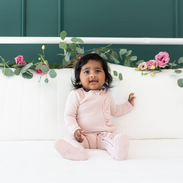Infant wearing Kyte Baby Ribbed Ruffle Zippered Footie Pajamas in Blush