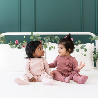 Babies wearing Kyte Baby Bamboo Ribbed Zippered Footie pajamas with Ruffle