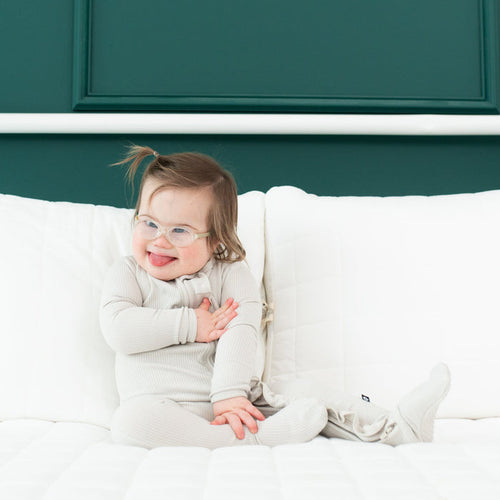 Toddler wearing Kyte Baby Ribbed Ruffle Zipper Footie in Oat