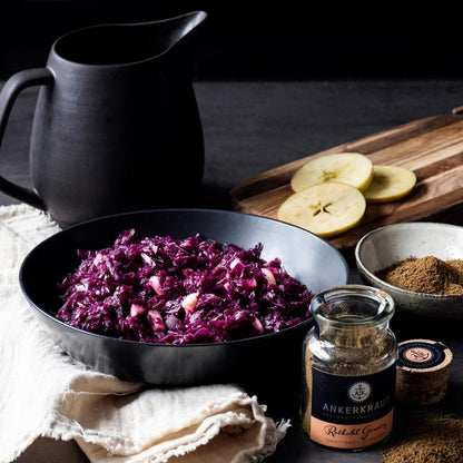 Rotkohl mit Apfelstücken in Schale, daneben Rotkohl Gewürz und frische Zutaten auf dunklem Tisch.