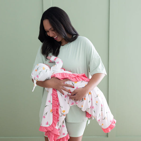 Mother holding her newborn wrapped in the Ruffle Baby Blanket in Tulip 0.5