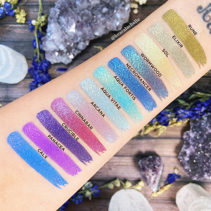 Top angled arm swatches on fair skin tone of Rune Duochrome Eyeshadow next to Elixir, Sol, Wormwood, Necromancer, Aqua Fortis, Aqua Vitae, Arcana, Cinnabar, Crucible, Panacea, Calx