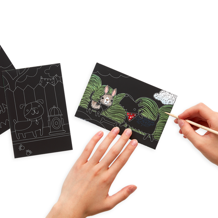 Hands scratching the Playful Pups Scratch and Scribble Mini Scratch Art Kit with the included wooden stylus