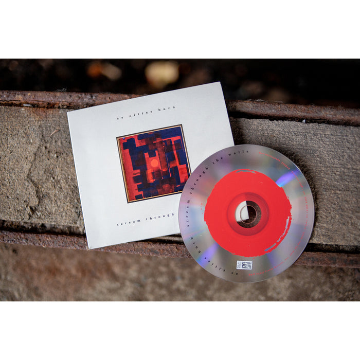 Shown is a CD case with a primarily white background, but a red square like shape in the center. There is small text on both above and below the red square like shape. Leaning on the CD case is the CD itself with a red and silver color. The background of this image is a rustic setting.