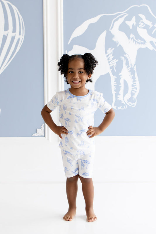 Young girl modeling the Short Sleeve Pajamas in Toile Safari standing in front of white and blue inspired art work