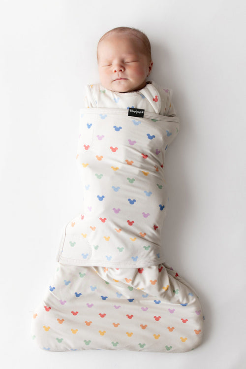 Newborn baby swaddled in a colorful mickey-patterned swaddle on a white background