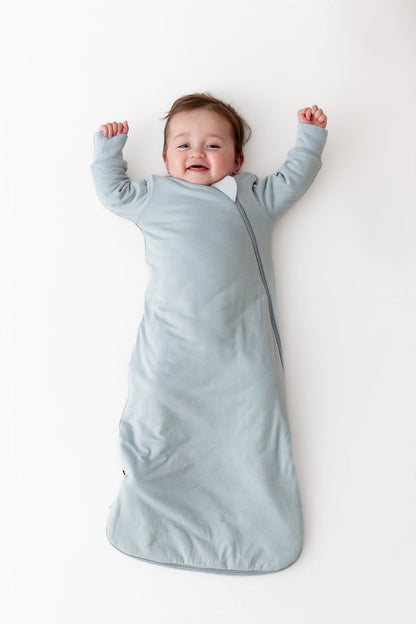 Baby wearing a long sleeve wearable blanket in a light blue color laying on a white surface