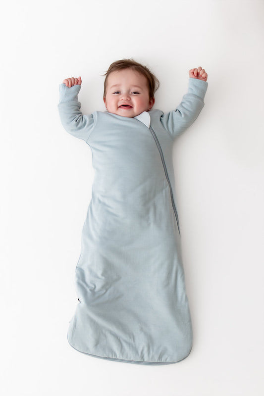 Baby wearing a long sleeve wearable blanket in a light blue color laying on a white surface