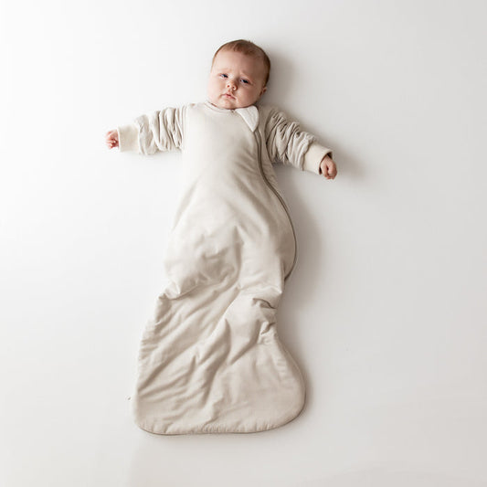 Baby in oat slumber bag on a neutral backdrop