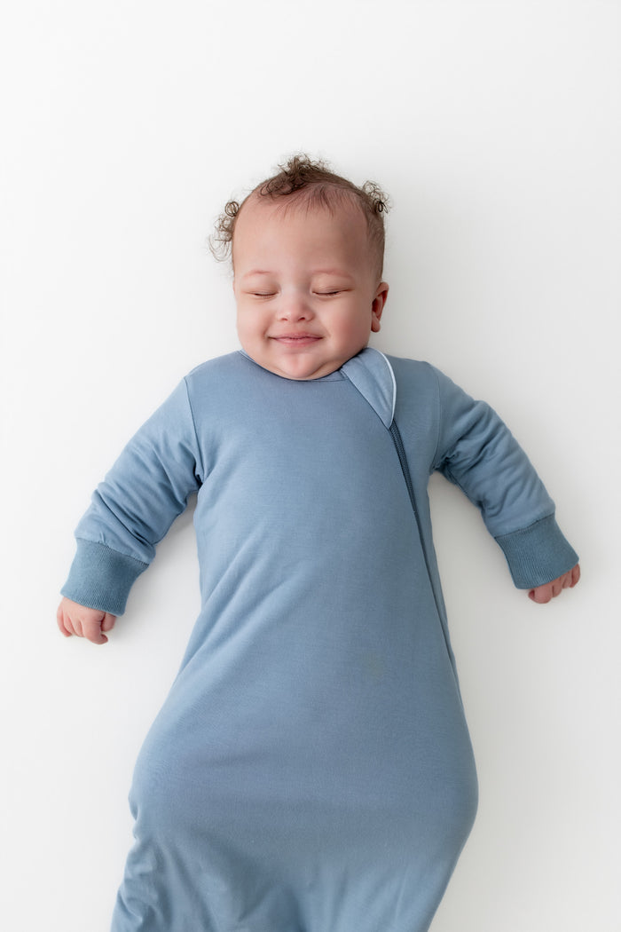 Baby in a blue slumber bag lying on a white surface