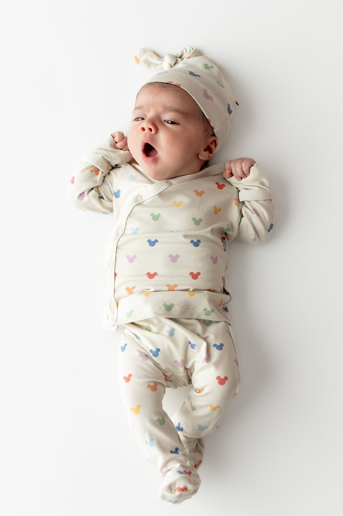 Baby wearing a colorful mickey outfit and hat on a white background