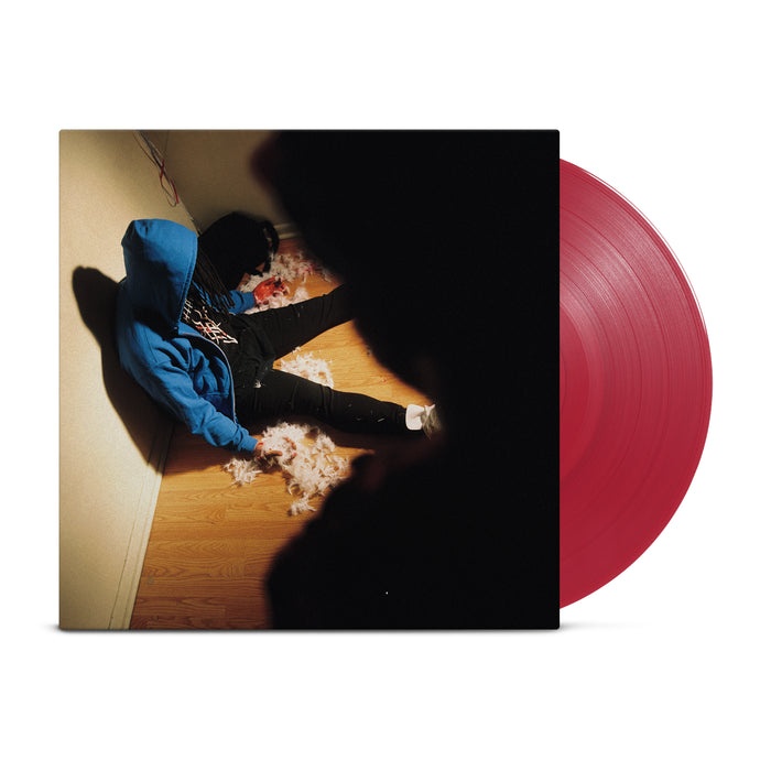 A red vinyl peeks out of a jacket with a picture of a man with a blue hoodie and dreads slumped over against a wall with a dark figure over him.