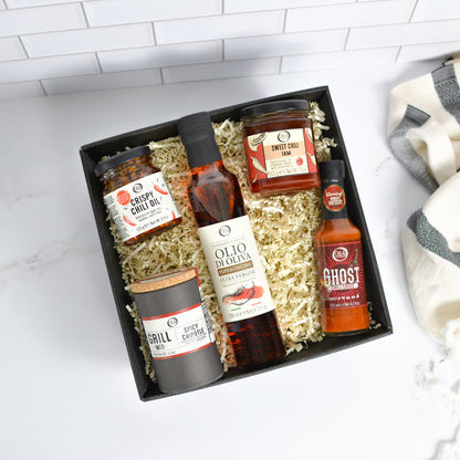 Gift box with various food products including bottles and jars on a white surface.