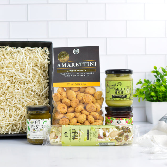 Assorted food items including Amarettini cookies, pesto spread, and other snacks on a white surface with a white tiled wall background.