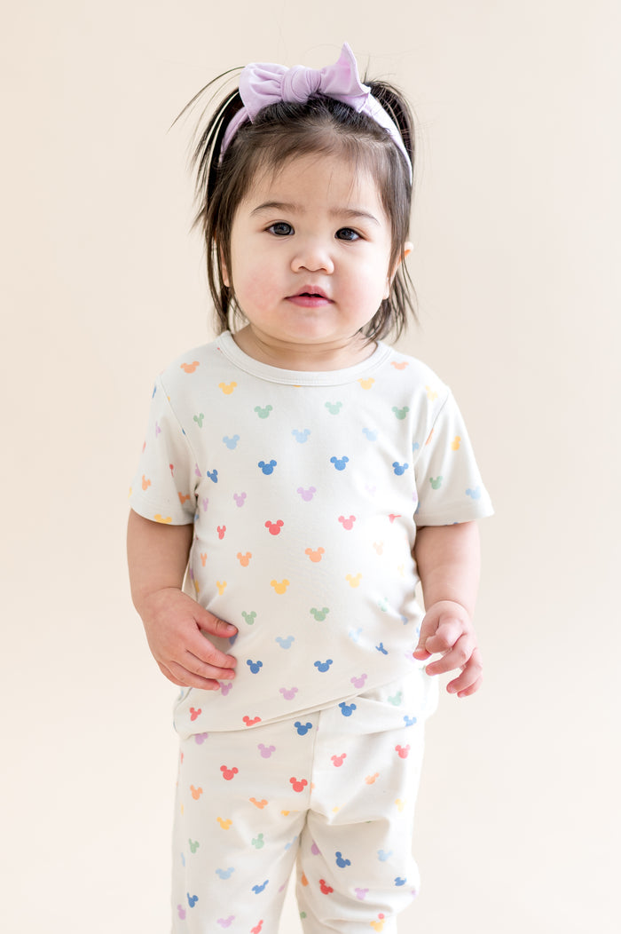Child wearing a white outfit with colorful mickey patterns on a plain background