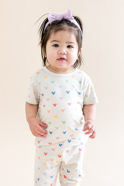 Child wearing a white outfit with colorful mickey patterns on a plain background