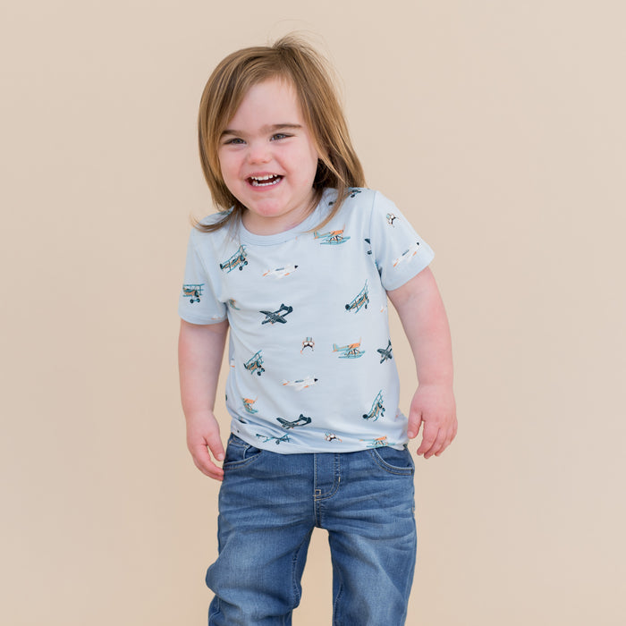 Smiling child wearing the Toddler Basic Tee in Take Off with medium wash jeans