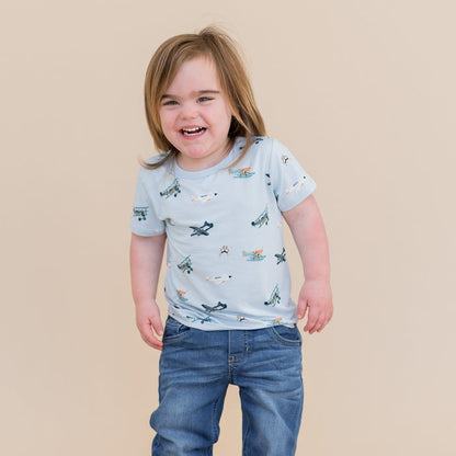 Smiling child wearing the Toddler Basic Tee in Take Off with medium wash jeans