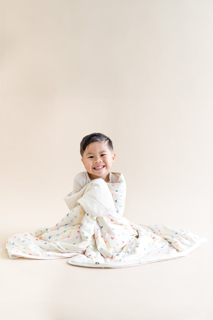 Child wrapped in a colorful blanket with mickey head pattern on a plain background