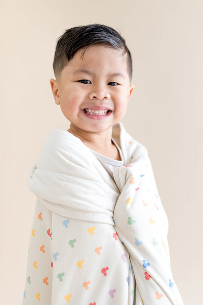 Child wrapped in a blanket with colorful patterns on a plain background