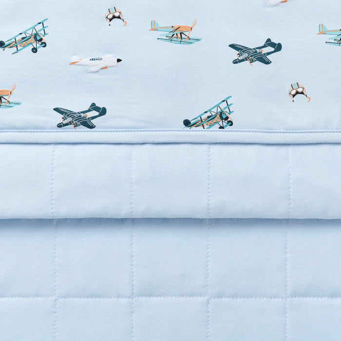 Close up of the Toddler Blanket in Take Off 1.0 showing the light blue quilted backing and plane print smooth top layer