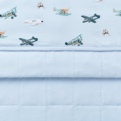 Close up of the Toddler Blanket in Take Off 1.0 showing the light blue quilted backing and plane print smooth top layer