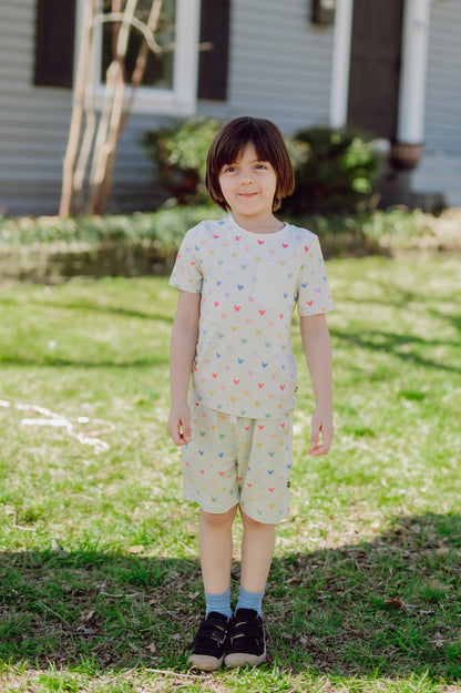 Child wearing a light-colored outfit with mickey patterns standing on grass.
