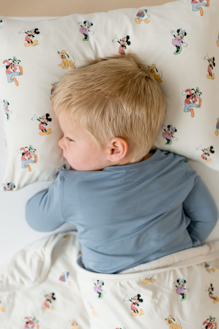 Child in a blue shirt lying on a bed with cartoon character bedding