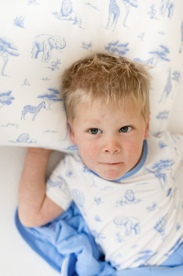 Young boy laying on a pillow with the Toddler Pillowcase in Toile Safari on it  underneath a matching blanket