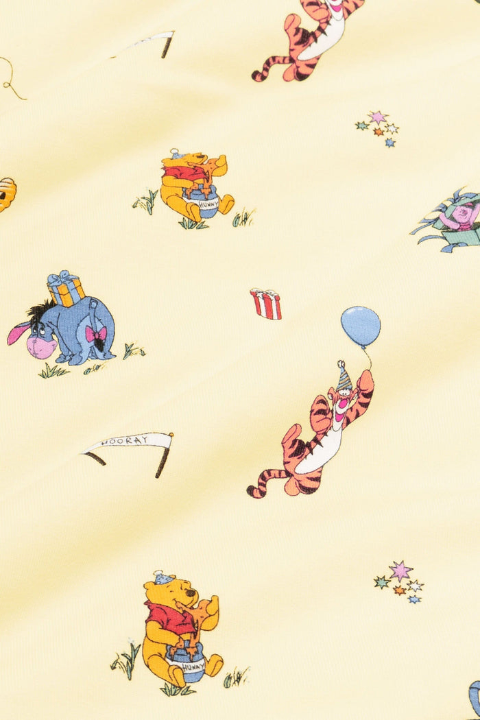Close up of fabric swatch of the Winnie the Pooh Celebration print  showing the story book characters on a yellow background