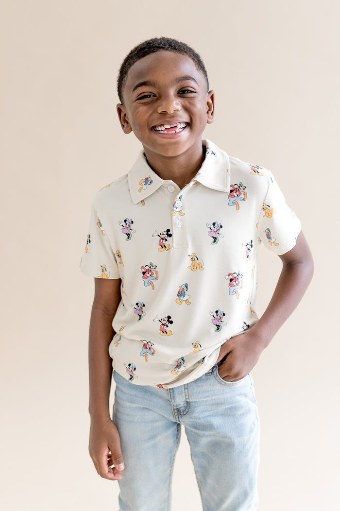 Child wearing a cream colored polo shirt with mickey and friends pattern and jeans