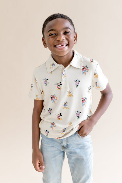 Child wearing a cream colored polo shirt with mickey and friends pattern and jeans